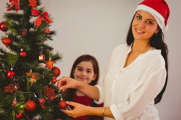 Mother and daughter hanging christmas decorations on tree