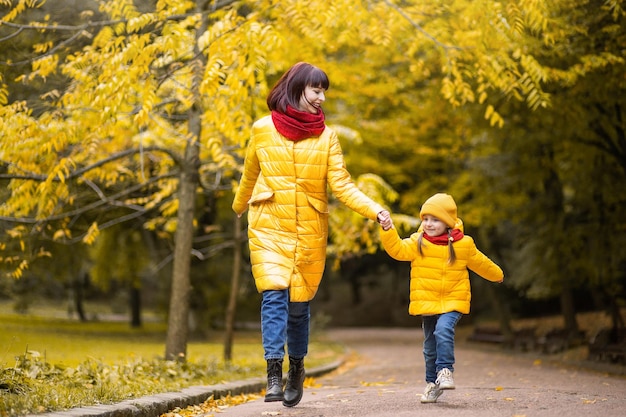 Mother and daughter having fun while running and laughing in the autumn park among the beautiful yellow trees. Happy family enjoying time together