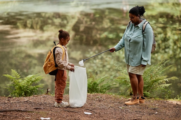 Mother and daughter helping clean nature and picking plastic bottles outdoors