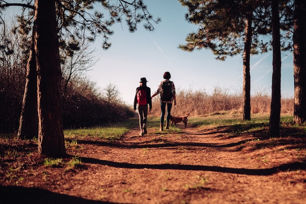 Mother and daughter hiking with dog on the pine forest trail