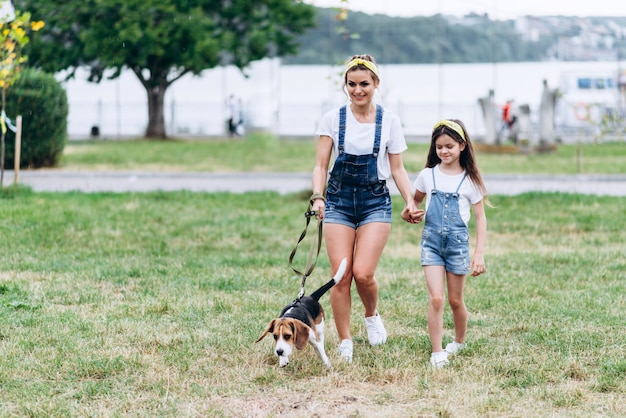 Mother and daughter holding hand to hand and walking with dog outdoor.