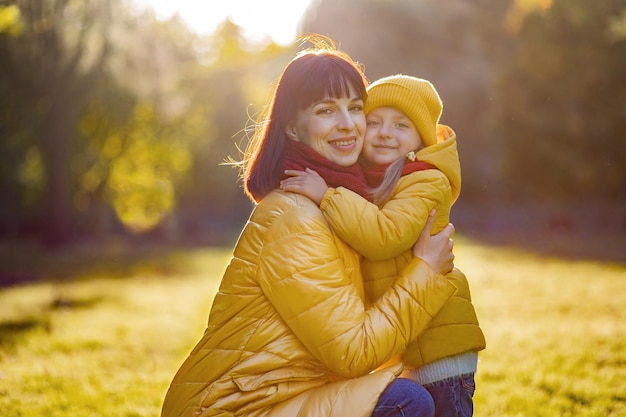 Mother and daughter hugging and smiling in autumn yellow park.