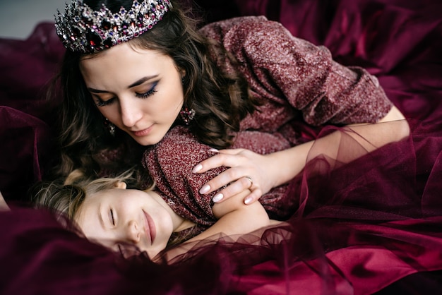 Mother and daughter in the image of the queen and princess dresses color Marsala lie together in bed, close-up, selective focus