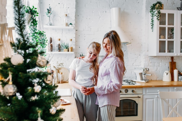 Mother and daughter in the kitchen decorated for Christmas, drinking tea or cocoa, conversation, waiting for guests