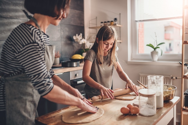 Mother and daughter kneading dough on the wooden table