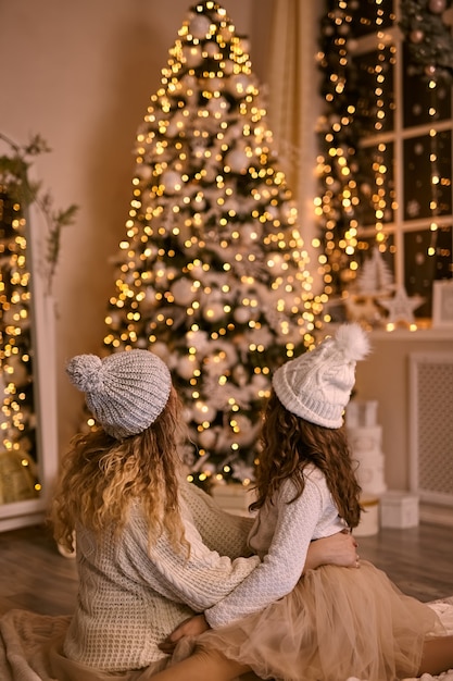 Mother and daughter in knitted hats looking at shining Christmas tree