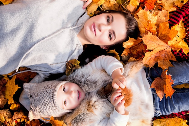 Mother and daughter lie on autumn leaves