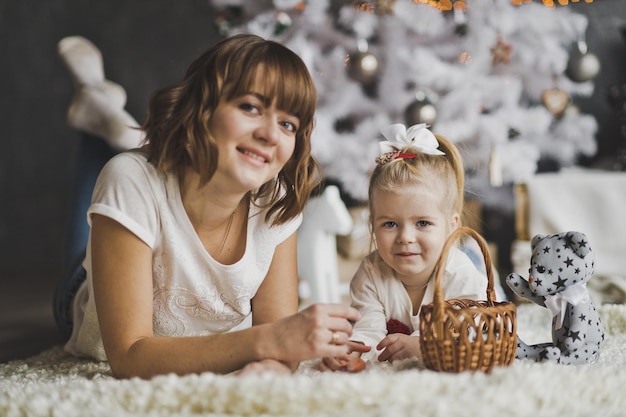 Mother and daughter lying on the carpet under white decorated Christmas tree 7129