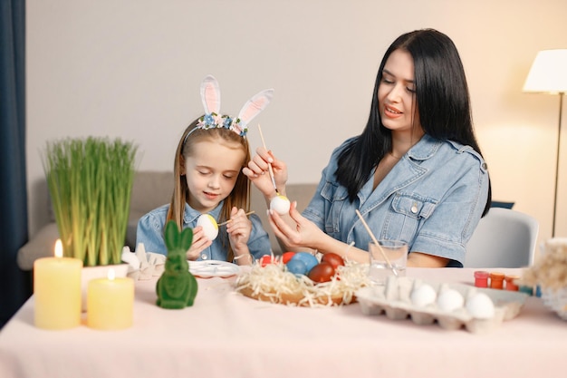 Mother and daughter in modern light kitchen and paining Easter eggs together