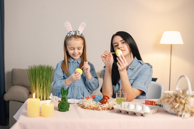 Mother and daughter in modern light kitchen and paining Easter eggs together