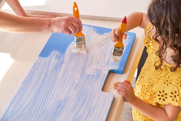 Mother and daughter painting a blue wood white with brushes