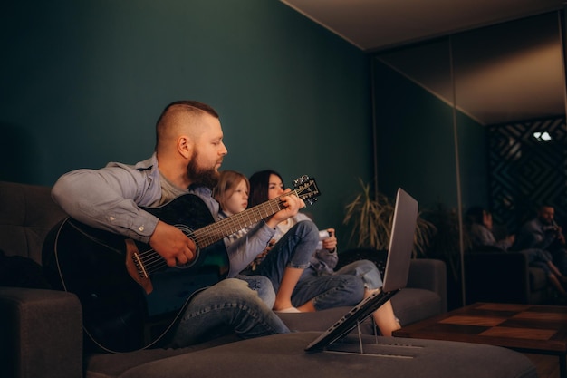 mother and daughter play a video game and father plays the guitar