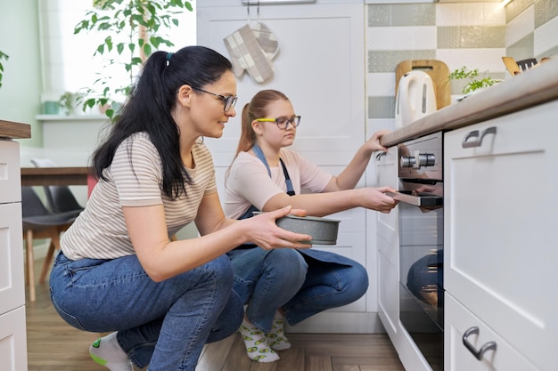 Mother and daughter preparing cake together putting mold with dough in oven