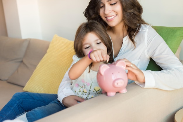 Mother and daughter putting coins into piggy bank