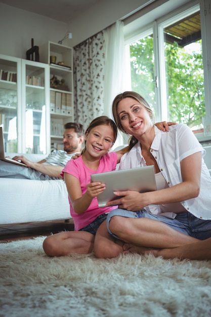 Mother and daughter sitting on floor and using digital tablet