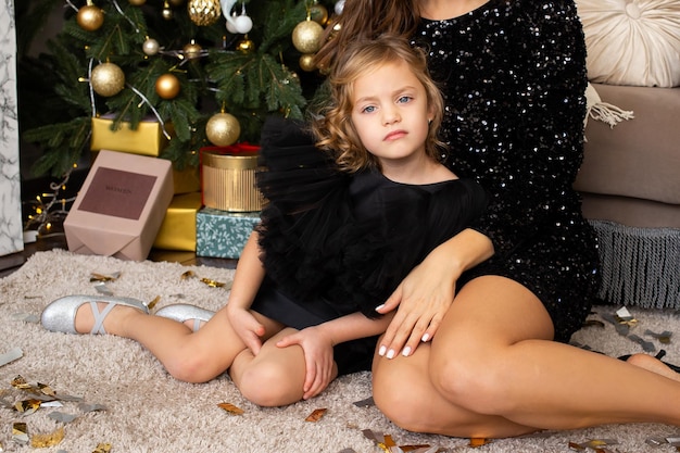 Mother and daughter sitting near Christmas tree at home Merry Christmas and Happy Holidays