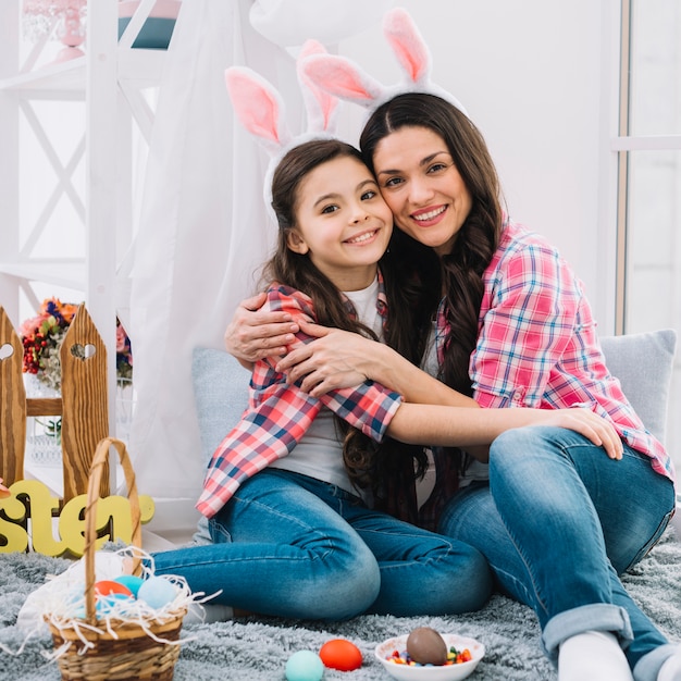 Mother and daughter sitting with easter eggs on bed embracing each other