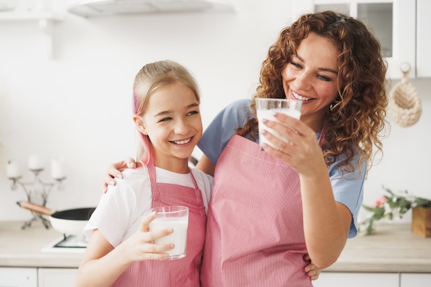 Mother and daughter smiling and holding glasses of milk in kitchen