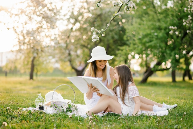 A mother and daughter in the spring garden on a plaid leaf through and look through a book with photos from a family photo shoot Remember the important moments of life in the photo album