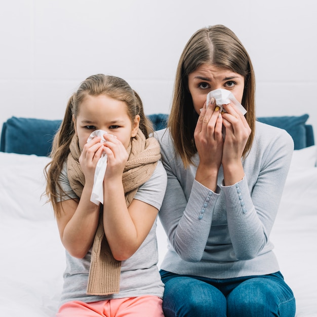 Mother and daughter suffering from cold and fever covering their nose with tissue paper