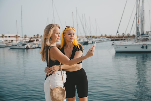 Mother and daughter take selfies against the background of the sea and yachts