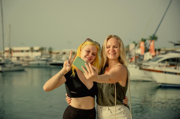 Mother and daughter take selfies against the background of the sea and yachts