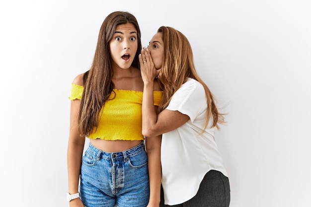 Mother and daughter together standing together over isolated background hand on mouth telling secret rumor whispering malicious talk conversation