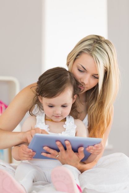 Mother and daughter using digital tablet on bed at home