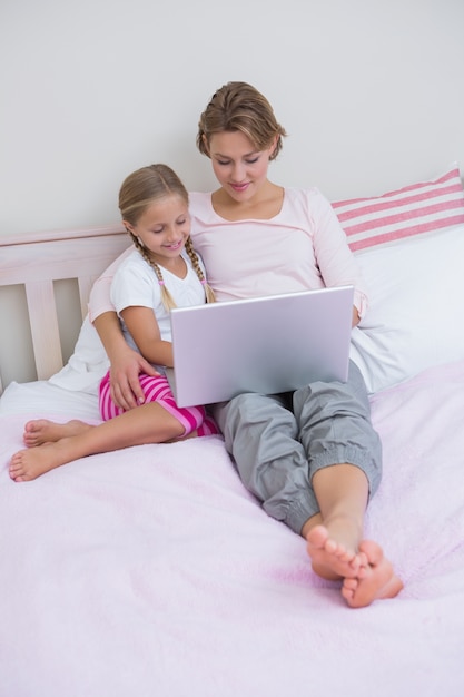 Mother and daughter using laptop in bed