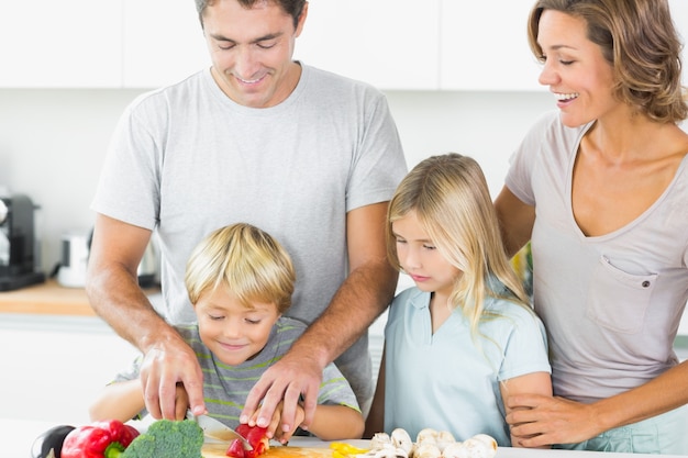 Mother and daughter watching father and son slicing vegetables