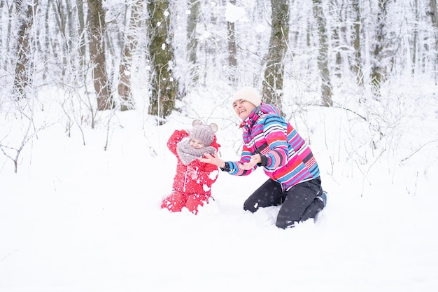 Mother and daughter on winter walk in nature. woman and child girl make snowman