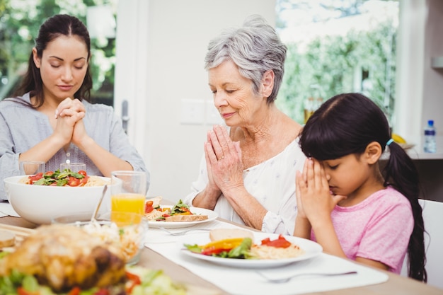 Mother and daughter with granny praying at dining table 