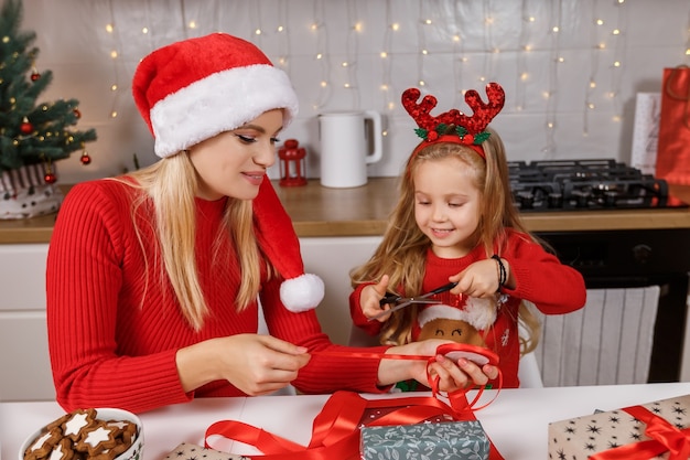 Mother and daughter wrapping christmas gift boxes on the background of decorated kitchen