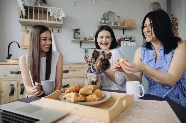 Mother and daughters talking and eating croissants in the kitchen