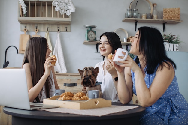 Mother and daughters talking and eating croissants in the kitchen