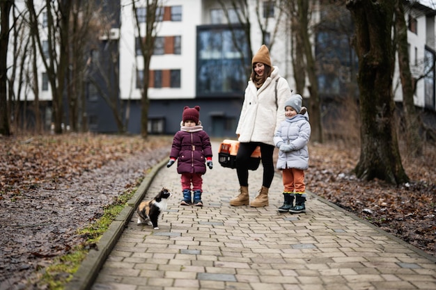 Mother and daughters walking with kitten in travel plastic cage carriage outdoor at park