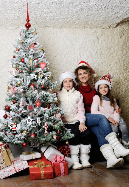 Mother and daughters with gifts near a christmas tree