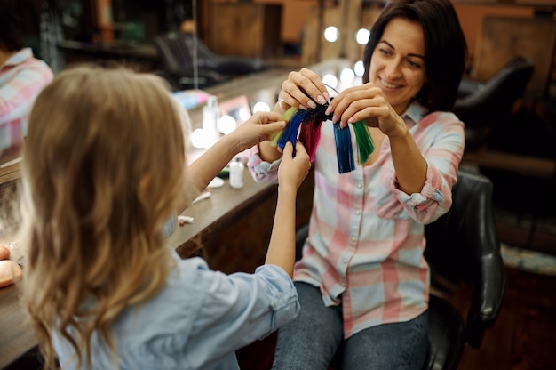 Mother doing hairstyle to her child in hairdressing salon