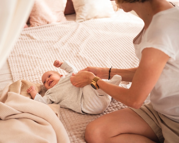 Mother dressing happy baby in bed