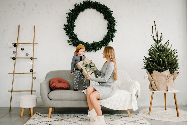 Mother exchanging gifts with daughter Parent and little child having fun near Christmas tree indoors Loving family with presents in room The morning before Xmas Portrait mom and child close up