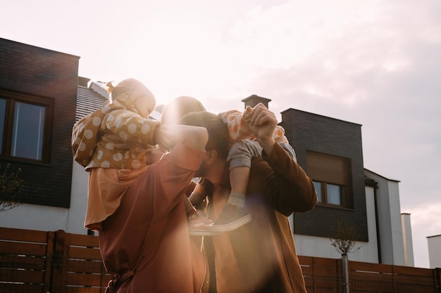 Mother father carrying children on piggyback near house on sunset