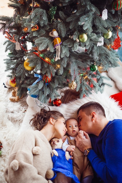 The mother,father,dog and baby lie on the floor  near Christmas Tree