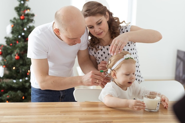 Mother and father helps to put on cochlear implant for their deaf baby daughter in christmas living room Hearing aid and innovating medical technologies treatment deafness concept