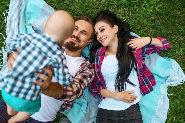 Mother, father and little baby lying on grass, top view