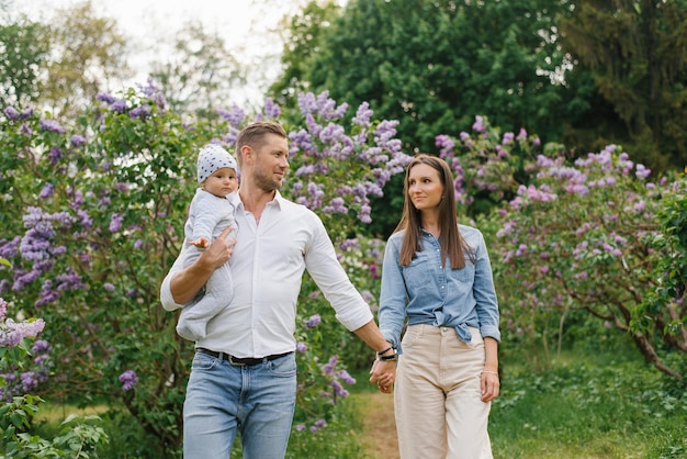 Photo mother father and little son are walking in a spring blooming park a happy mom and dad with a small child are having fun near the lilac the concept of a happy family