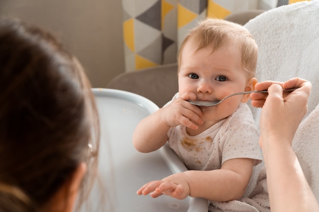 Mother feeding baby with spoon at home