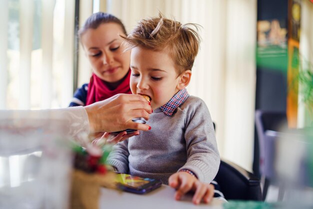 Photo mother feeding food to son while sitting with friend at restaurant