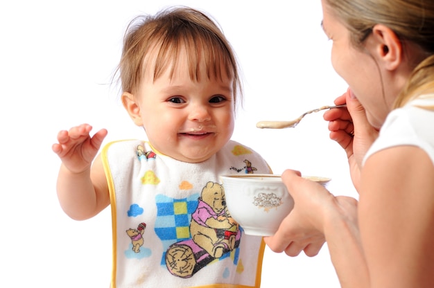 Mother feeds little one year girl of baby food or porridge with spoon