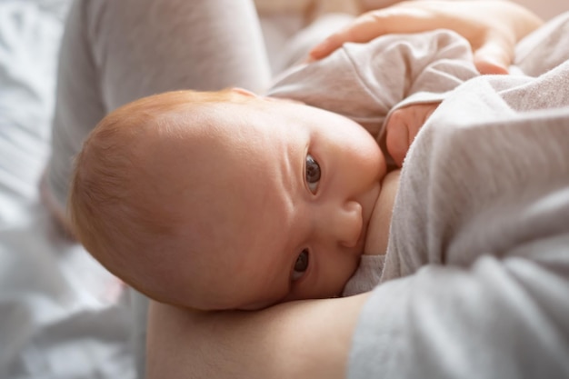 Mother feeds newborn baby girl with breast lying on bed