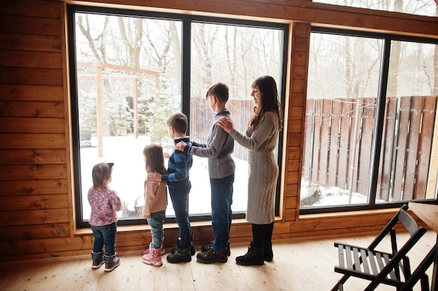 Mother and four kids in modern wooden house against large window